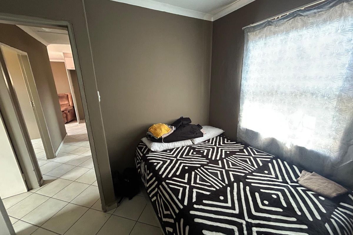 A bedroom featuring tiled flooring and neutral wall tones, with a view leading into the adjacent hallway.