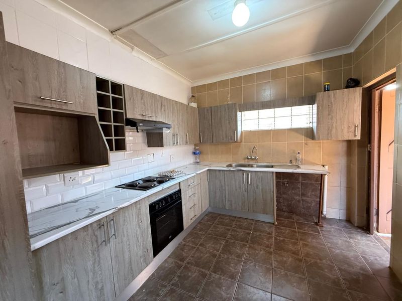 A functional kitchen featuring wood-look cabinetry, built-in oven and hob, tiled backsplash, and tiled flooring, offering a practical layout for culinary activities.