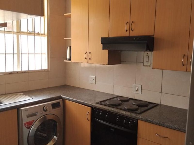 Functional kitchen featuring wood-look cabinetry, granite-style countertops, integrated oven and hob, and a tiled backsplash with security-barred window.