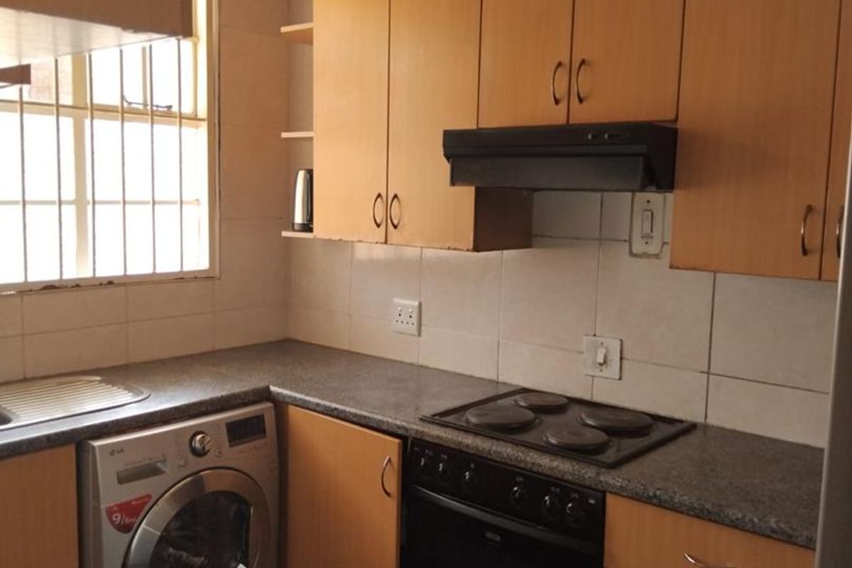 Functional kitchen featuring wood-look cabinetry, granite-style countertops, integrated oven and hob, and a tiled backsplash with security-barred window.
