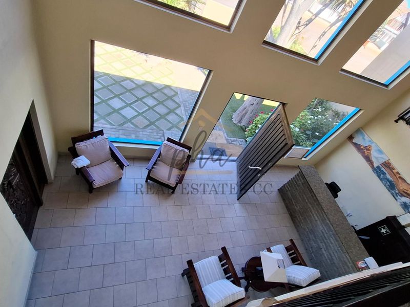 Spacious double-volume living area featuring large windows, tiled flooring, and a distinctive stone-clad feature wall, offering a bright and airy atmosphere.