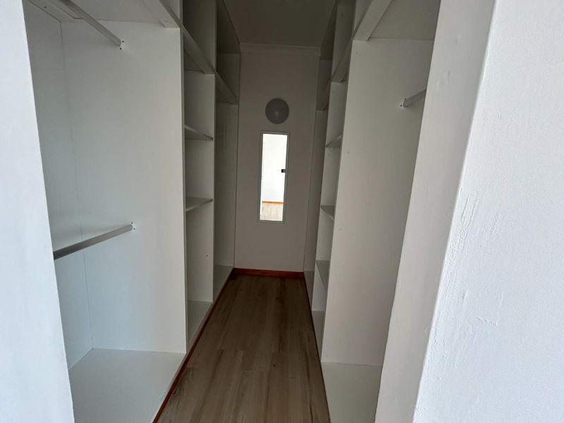 A walk-in closet or dressing area featuring built-in white shelving, hanging rails, and modern laminate flooring.
