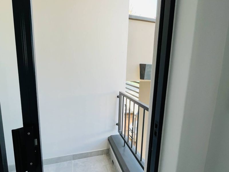 A compact, modern balcony featuring clean tiled flooring, a secure metal balustrade, and a sliding door entrance.