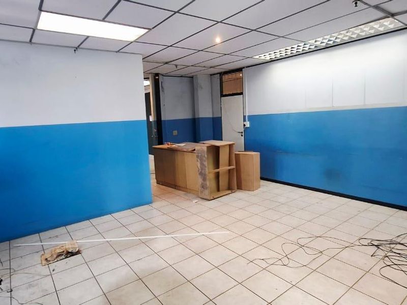 An empty office space featuring tiled flooring, a suspended ceiling with integrated lighting, and blue and white painted walls.