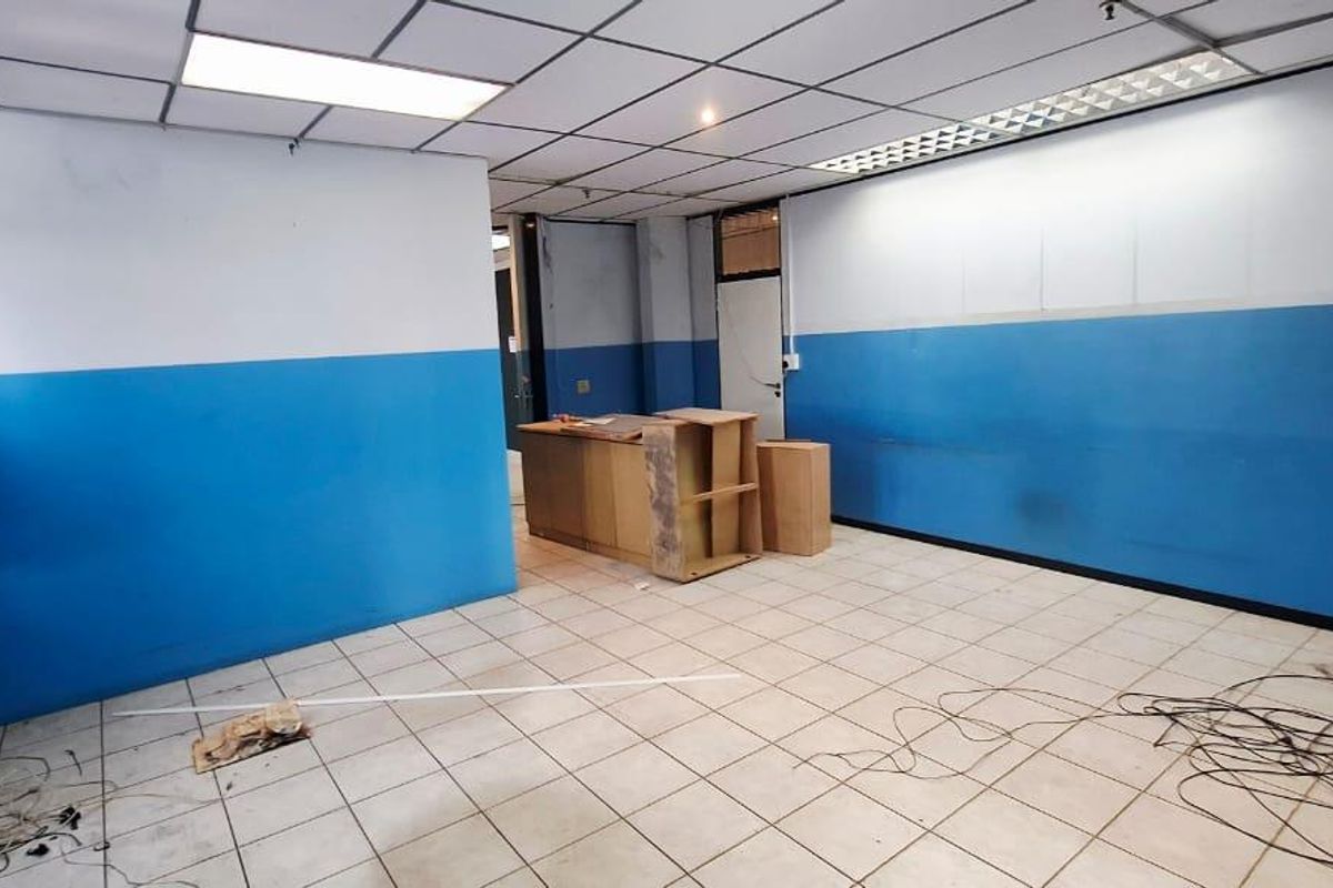 An empty office space featuring tiled flooring, a suspended ceiling with integrated lighting, and blue and white painted walls.