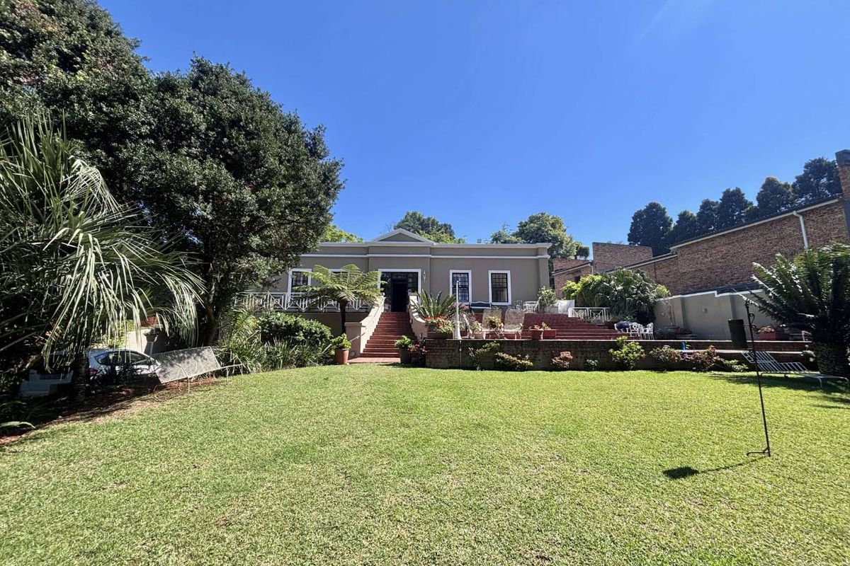 A spacious rear garden featuring a well-maintained lawn, a raised brick patio, and a grand staircase leading to the main house entrance.