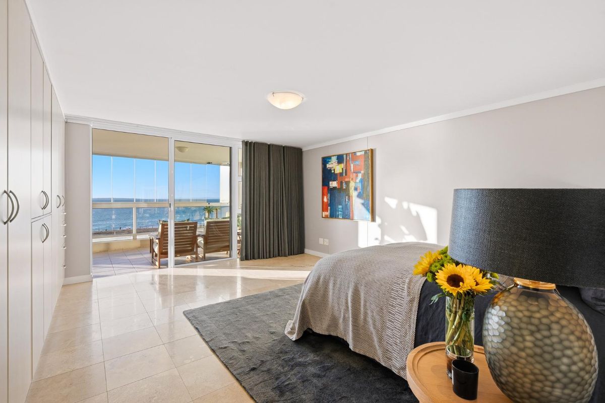 Spacious bedroom featuring built-in cupboards, tiled flooring, and large sliding glass doors opening onto a balcony with ocean views.
