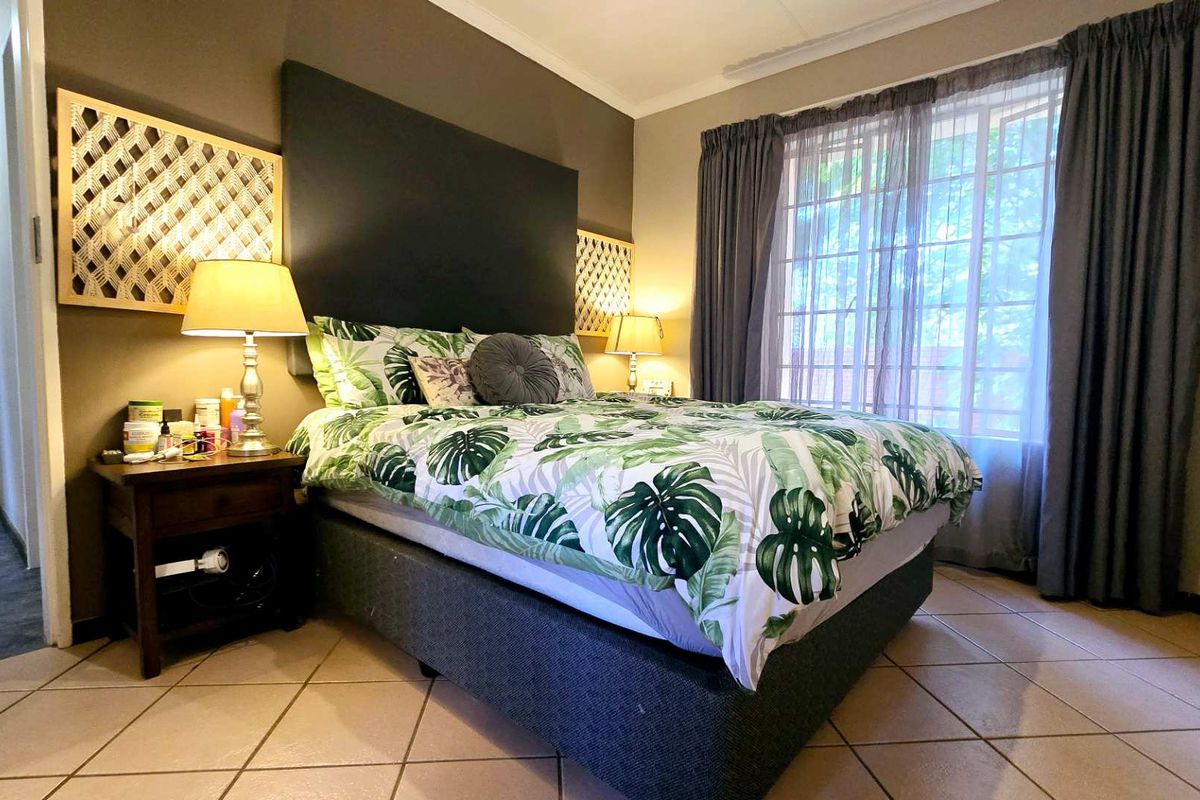 A well-lit bedroom featuring tiled flooring, a built-in headboard feature wall, and large windows with curtain tracks.