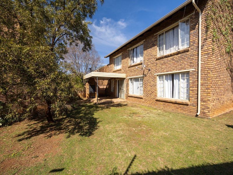 Rear view of a face brick apartment building featuring a covered patio area with a built-in braai and a private garden space.