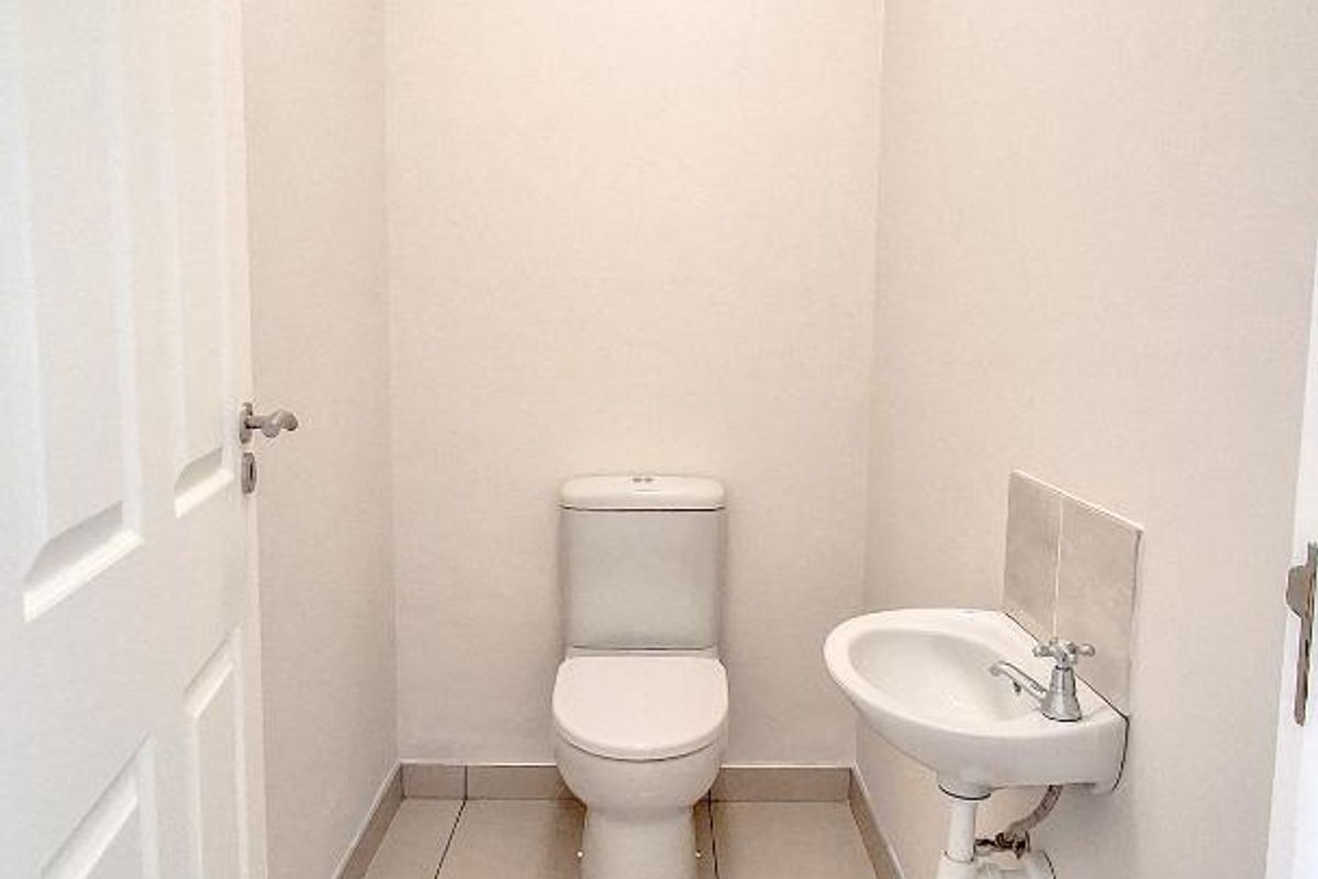 A clean and functional guest bathroom featuring a modern toilet and a wall-mounted basin with tiled flooring.