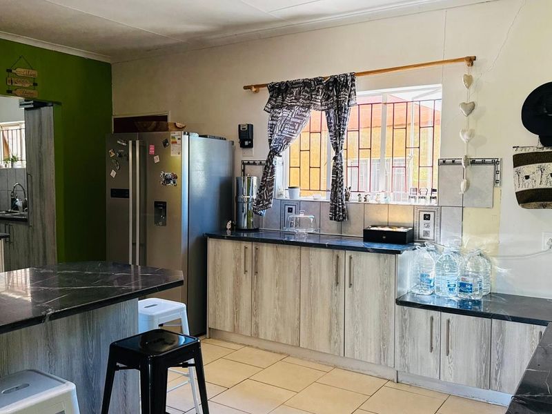 A functional kitchen featuring wood-look cabinetry, dark laminate countertops, tiled backsplash, and tiled flooring, with security bars installed on the window.