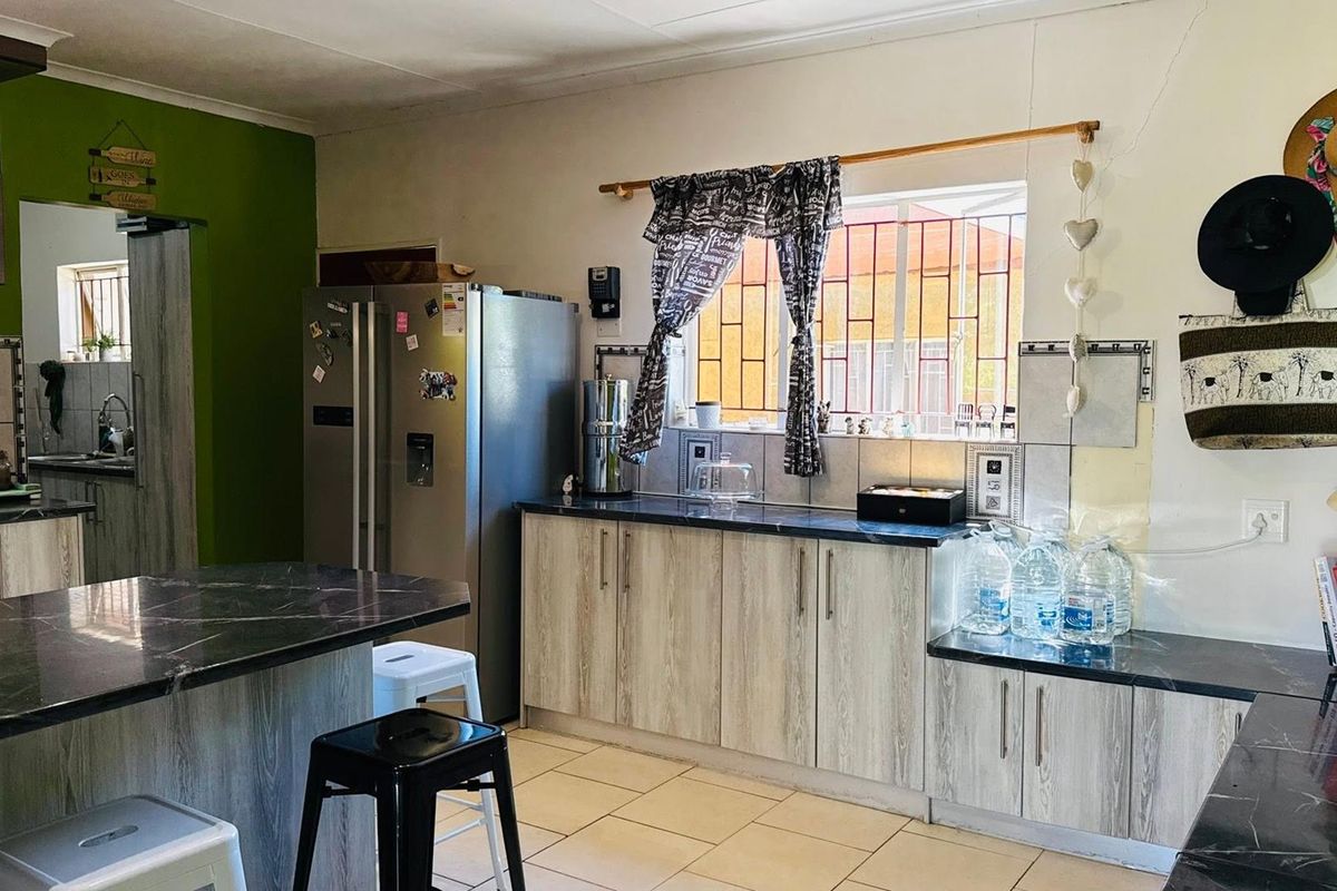 A functional kitchen featuring wood-look cabinetry, dark laminate countertops, tiled backsplash, and tiled flooring, with security bars installed on the window.