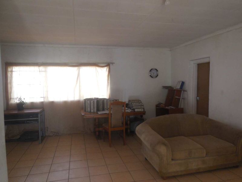 A living area featuring tiled flooring and a window, currently used as a workspace. The room requires cosmetic updates to improve its overall condition.