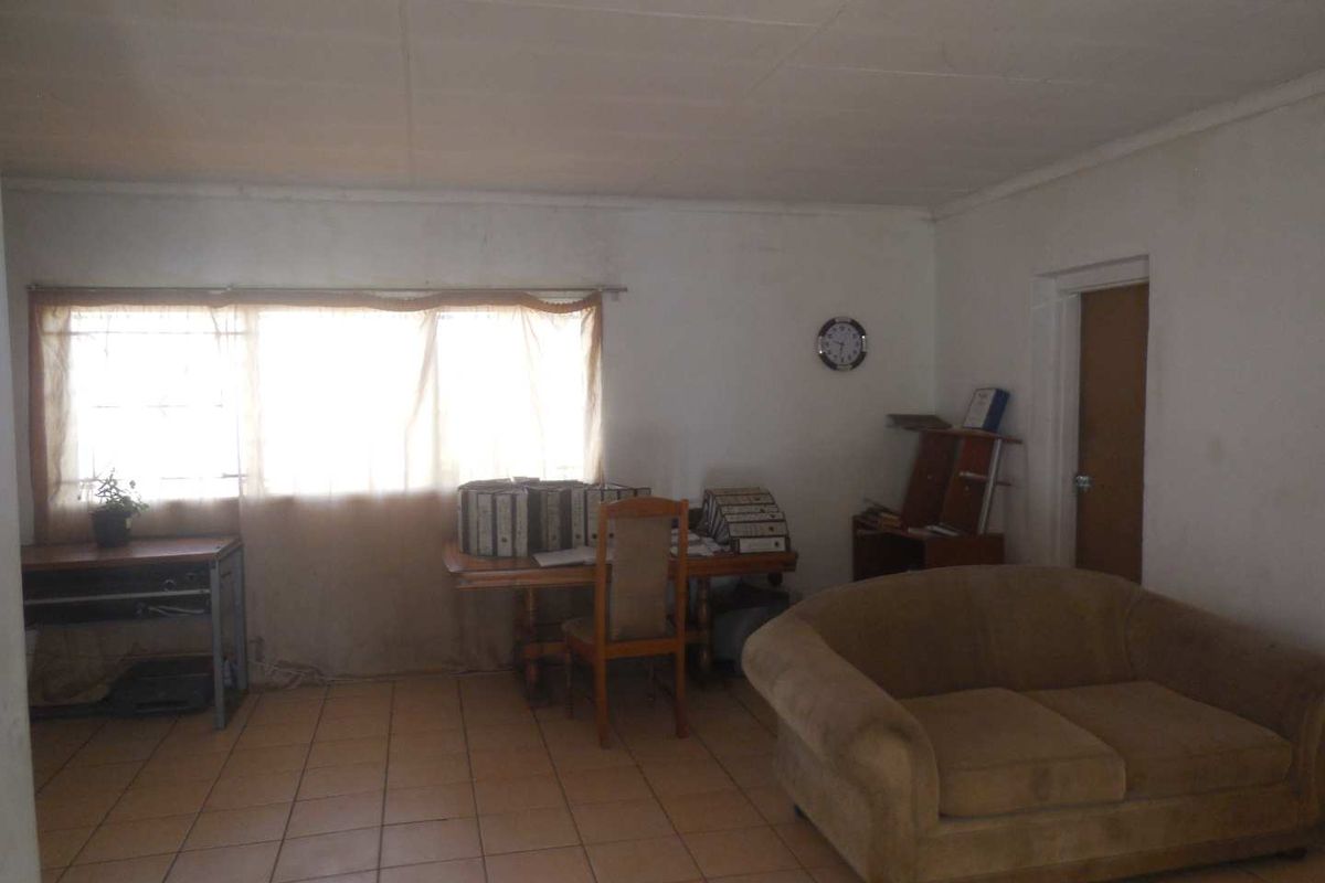 A living area featuring tiled flooring and a window, currently used as a workspace. The room requires cosmetic updates to improve its overall condition.