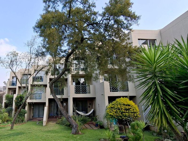 Rear view of a multi-story apartment complex featuring private balconies, sliding glass doors, and a well-maintained communal garden area.