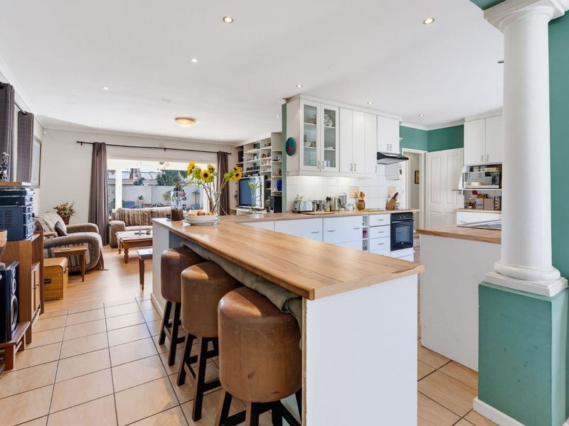 Open-plan living and kitchen area featuring a breakfast bar, white cabinetry, built-in oven, and tiled flooring, creating a functional and connected family space.