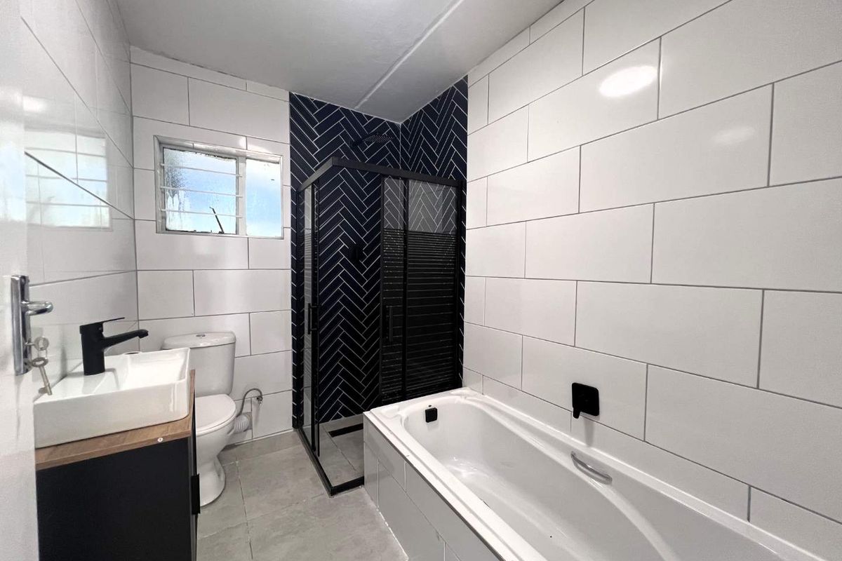 Modern bathroom featuring a white bathtub, a separate shower enclosure with dark herringbone tiling, a vanity basin, and a toilet.