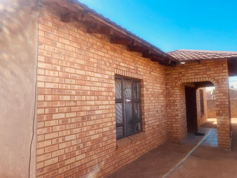 Exterior view of a face brick house featuring an arched entrance, tiled roof, and security bars on the windows.
