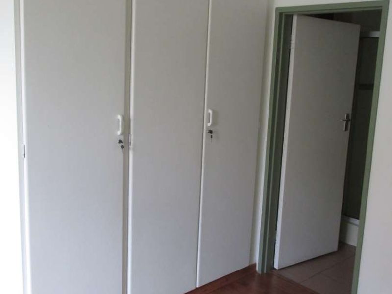 A clean bedroom featuring built-in cupboards and laminate flooring, with an adjacent doorway leading to another room.