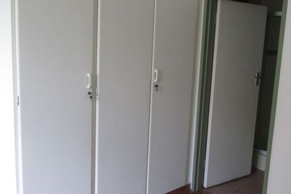A clean bedroom featuring built-in cupboards and laminate flooring, with an adjacent doorway leading to another room.