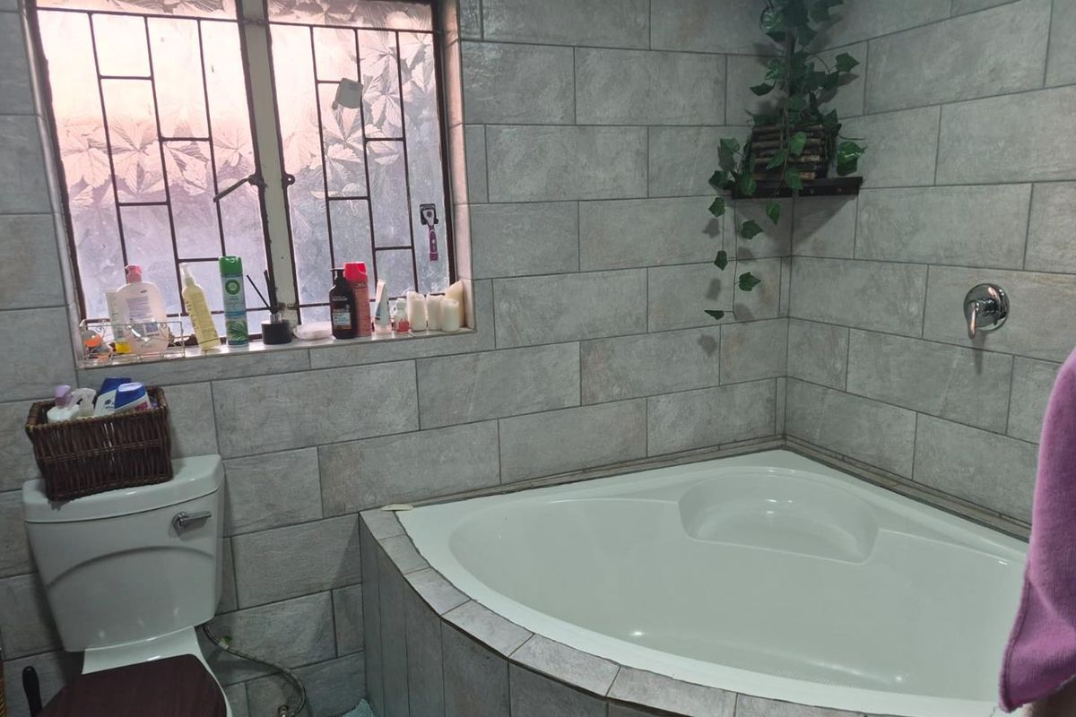A functional bathroom featuring a corner bathtub, tiled walls, and a window with security bars.