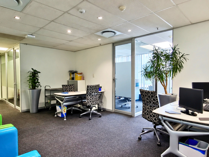 A professional office space featuring glass partitions, suspended ceilings with recessed lighting, and carpeted flooring, providing a functional and bright work environment.