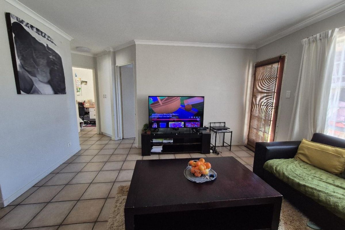 A functional living room featuring tiled flooring, neutral wall tones, and direct access to adjacent rooms and an exterior door.