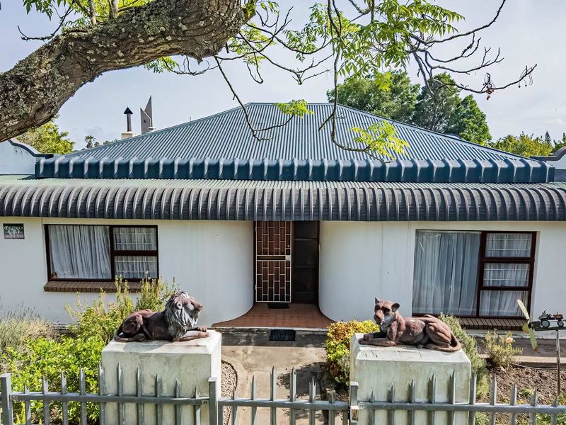 Front elevation of a single-story house featuring a corrugated metal roof, metal security gate, and a fenced garden entrance.