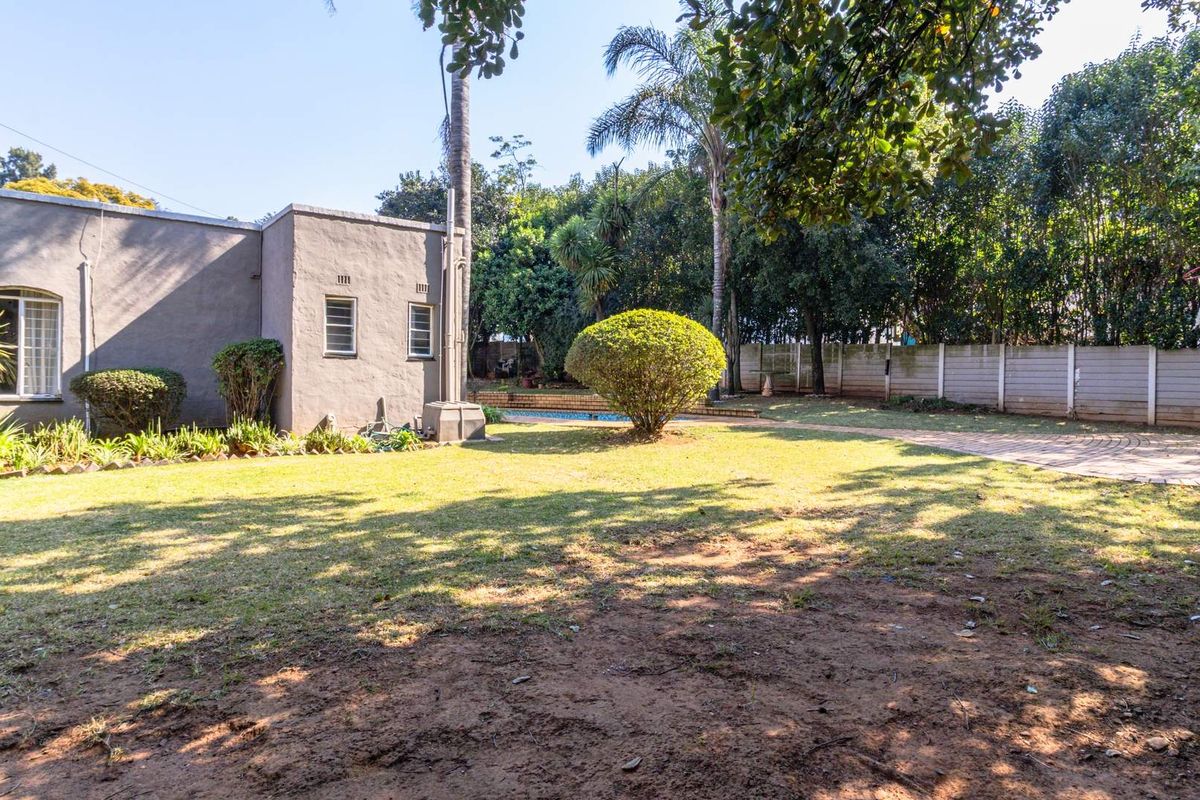 Spacious rear garden featuring a lawn, paved area, and swimming pool, enclosed by a precast concrete boundary wall.