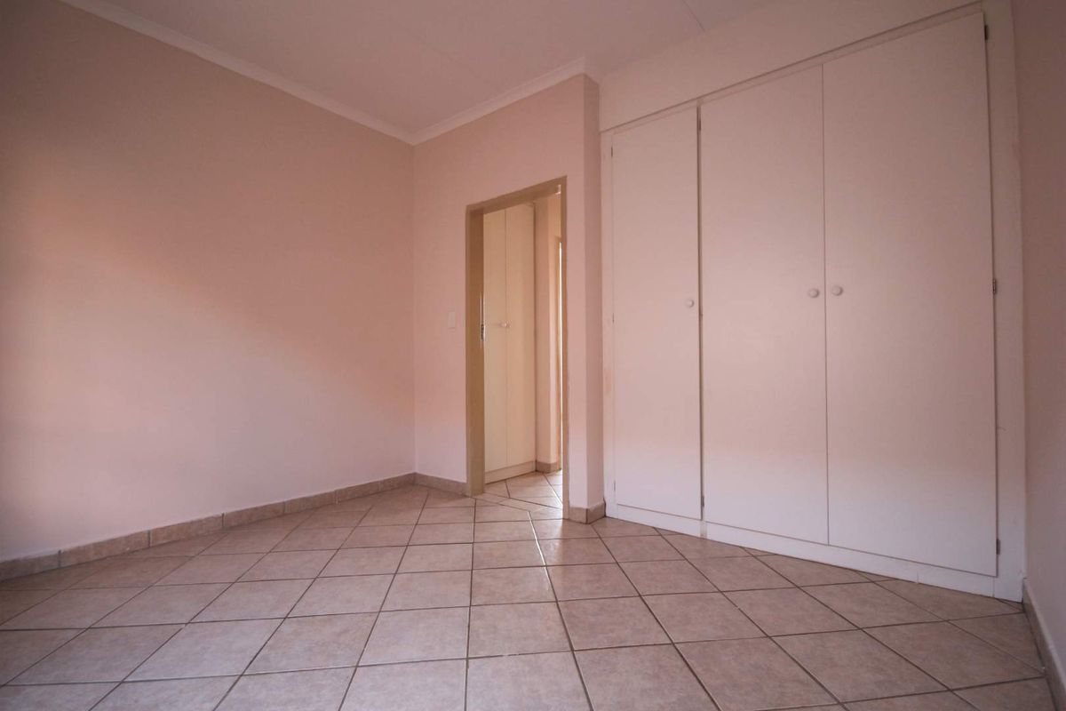 An empty bedroom featuring neutral wall paint, tiled flooring, and built-in storage cupboards.