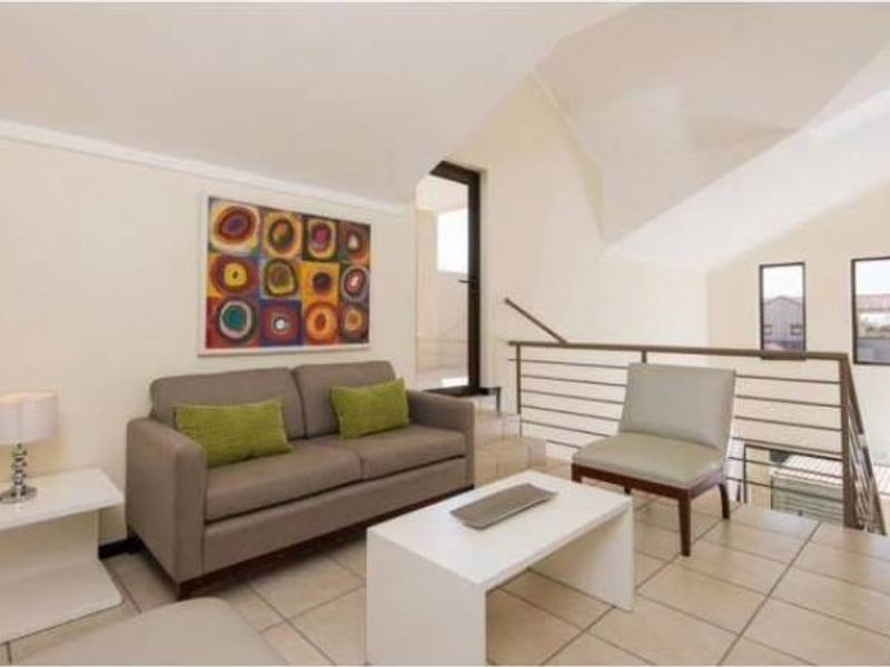 A bright living area featuring tiled flooring, a metal balustrade, and a sloped ceiling with a skylight, creating an open and airy atmosphere.