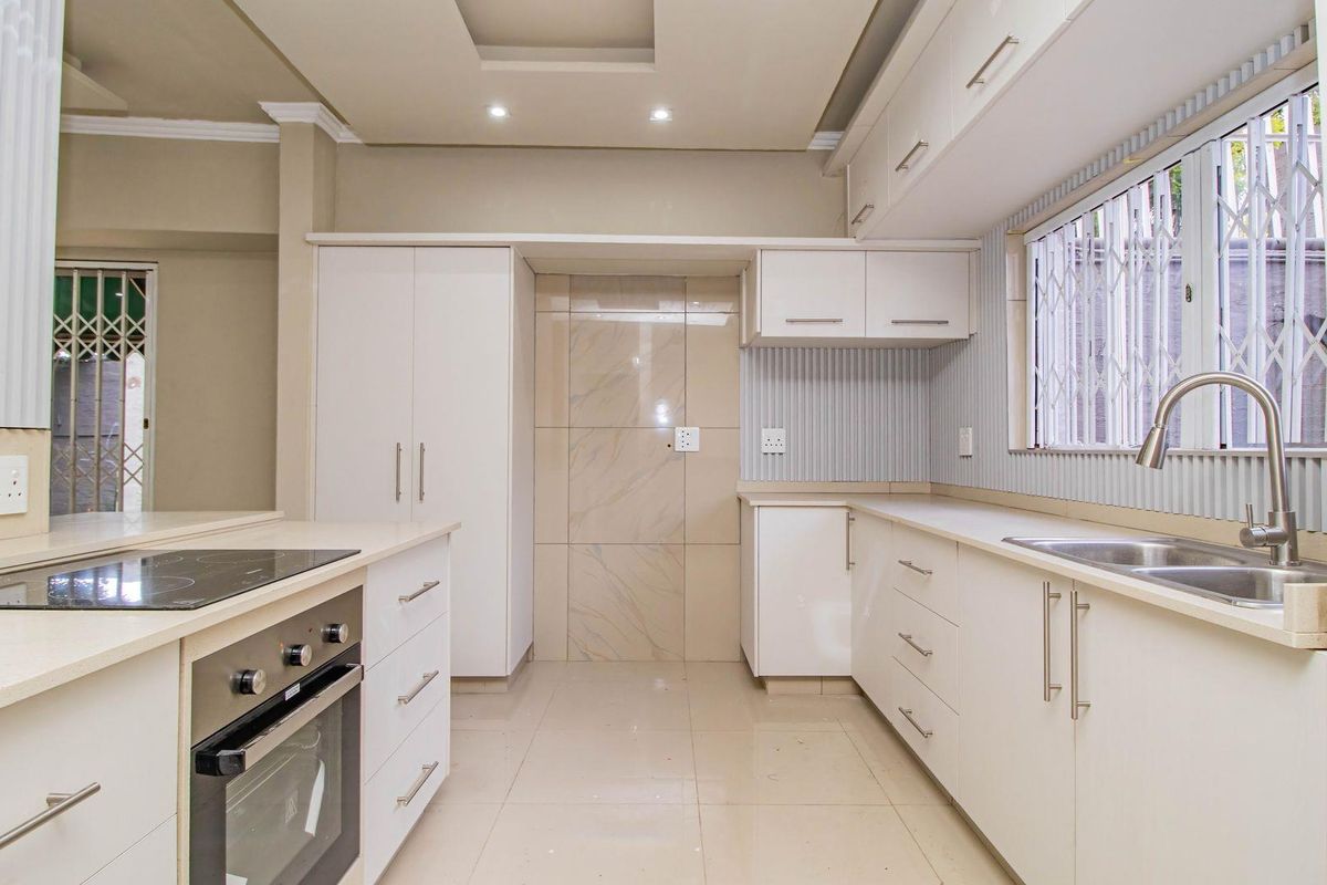 Modern kitchen featuring white cabinetry, stone countertops, integrated oven, electric hob, and a stainless steel sink with a gooseneck faucet.