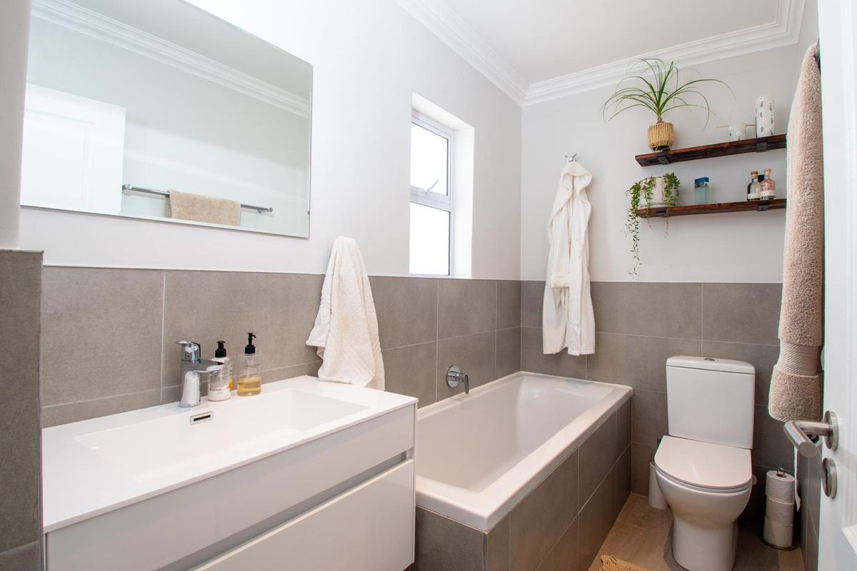 A modern bathroom featuring a white vanity with integrated basin, a built-in bathtub with grey tiling, and a standard toilet.