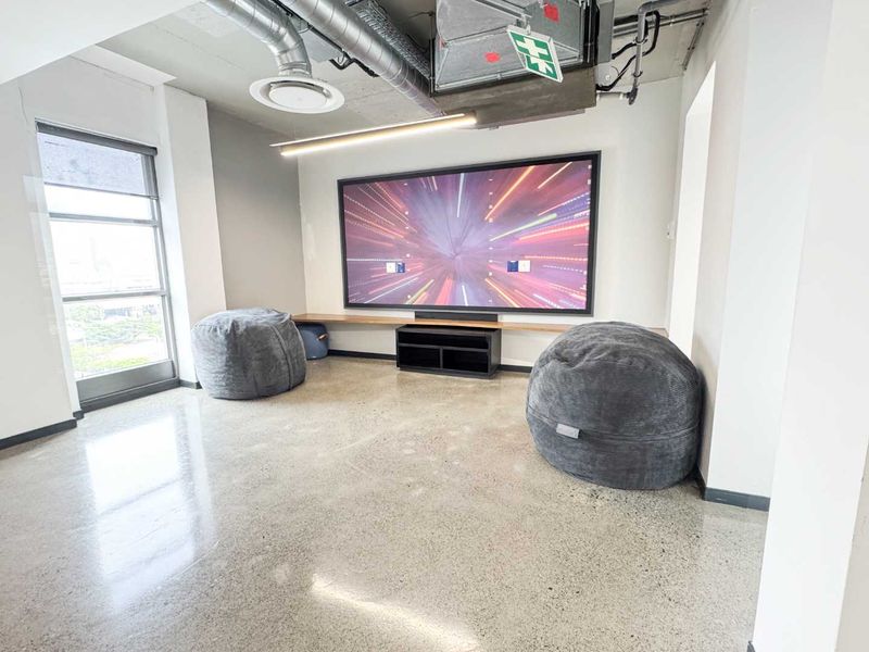 Modern cinema room featuring polished concrete floors, exposed industrial ceiling with ducting, and a large built-in wall screen for immersive viewing.