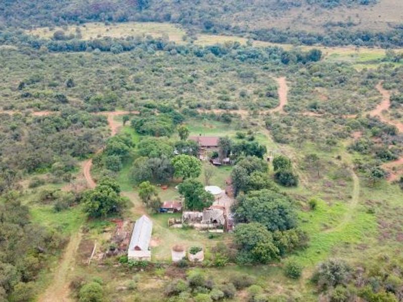 Aerial view of a rural farm property featuring multiple outbuildings, water storage tanks, and surrounding natural bushveld landscape.