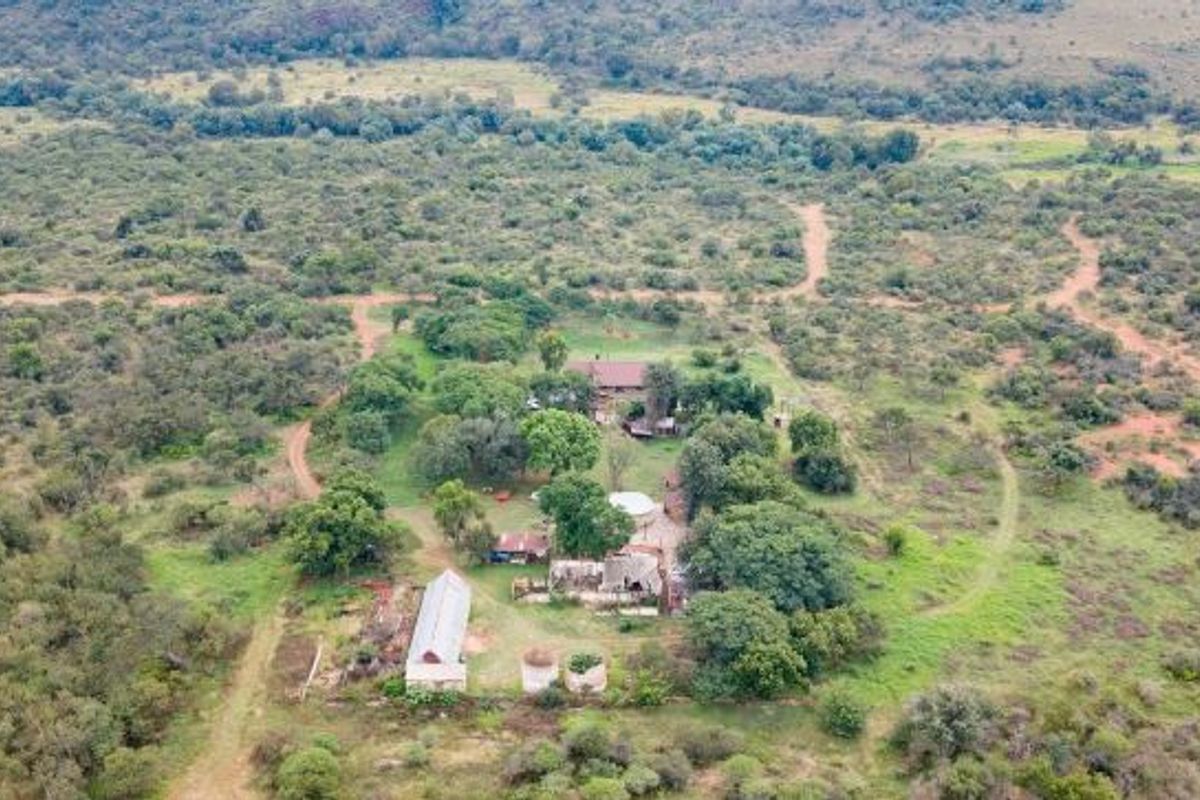 Aerial view of a rural farm property featuring multiple outbuildings, water storage tanks, and surrounding natural bushveld landscape.