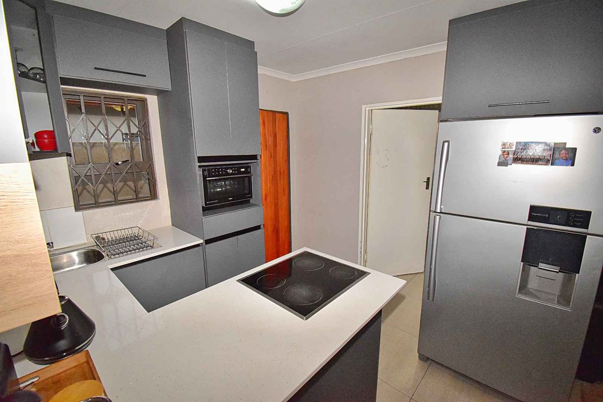 Modern kitchen featuring grey cabinetry, stone countertops, a built-in oven, and a central island with an integrated electric hob.