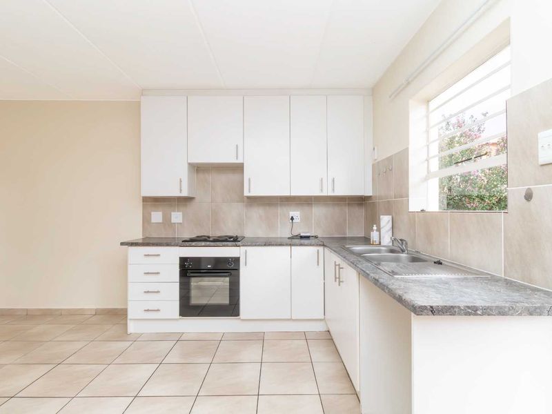 A clean, functional kitchen featuring white cabinetry, laminate countertops, a built-in oven with gas hob, and neutral tiled flooring and splashbacks.