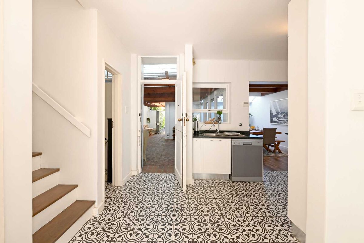 A bright kitchen area featuring patterned floor tiles, built-in cabinetry, a stainless steel sink, and an integrated dishwasher, with access to an outdoor patio.