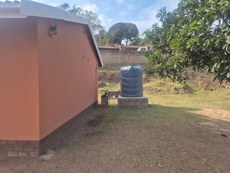 Rear exterior view showing a water storage tank on a concrete plinth with an integrated water pump system adjacent to the house wall.