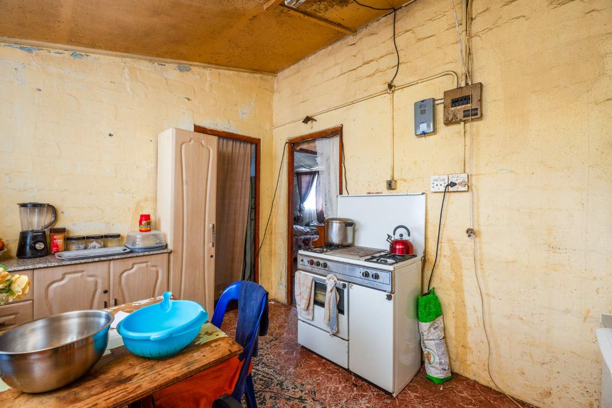 A dated kitchen area featuring basic cabinetry, a freestanding stove, and exposed electrical wiring, requiring significant renovation and cosmetic updates.