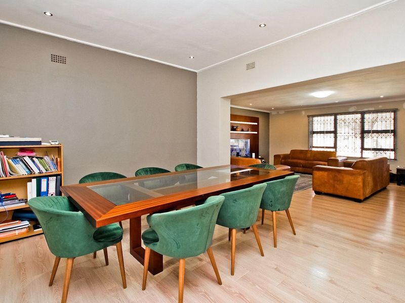 Spacious open-plan dining and living area featuring light laminate flooring, recessed lighting, and a neutral color palette with a built-in shelving unit.