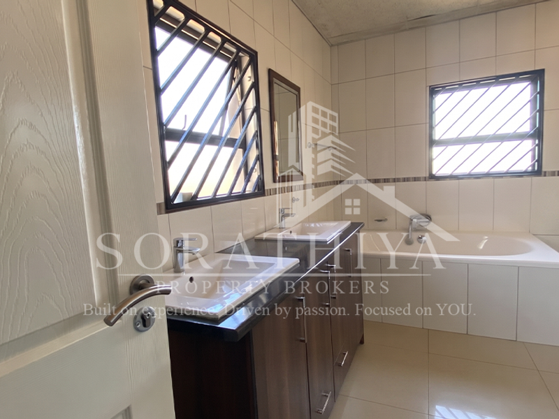 A spacious bathroom featuring a double vanity, built-in bathtub, and toilet, finished with neutral wall and floor tiles.