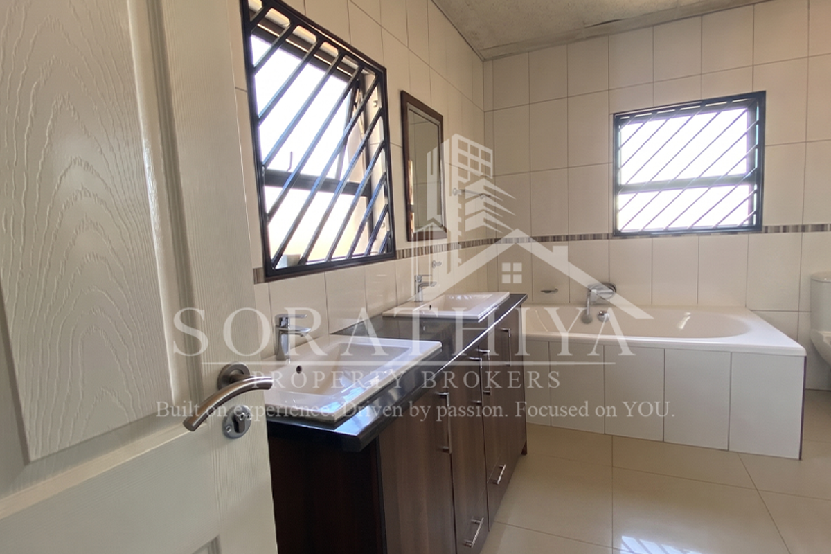 A spacious bathroom featuring a double vanity, built-in bathtub, and toilet, finished with neutral wall and floor tiles.
