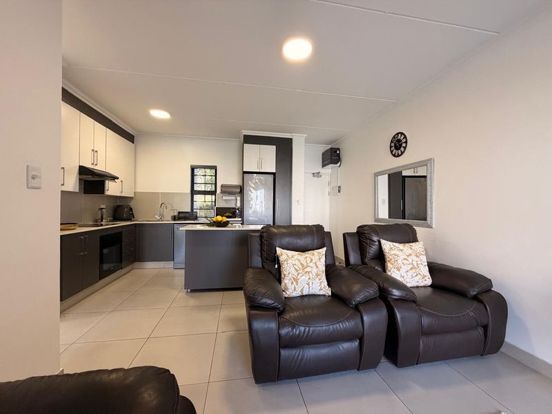Modern open-plan kitchen and living area featuring sleek two-tone cabinetry, integrated appliances, a central kitchen island, and neutral tiled flooring throughout.