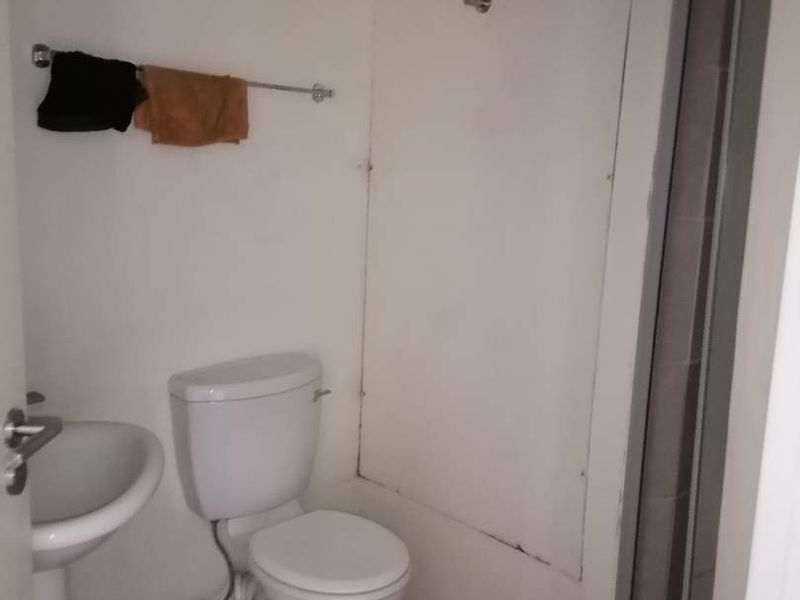 A compact bathroom featuring a pedestal basin, toilet, and shower enclosure, requiring cosmetic updates to improve its overall condition and appeal.
