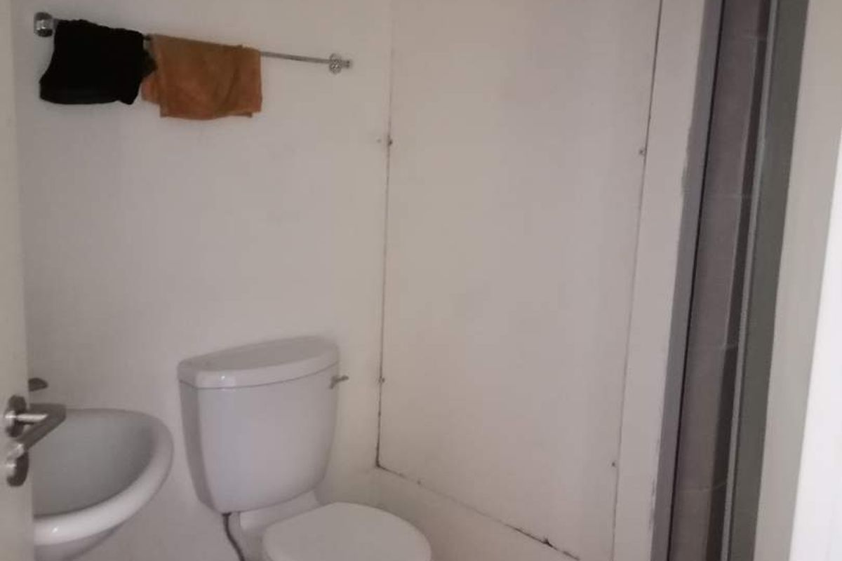 A compact bathroom featuring a pedestal basin, toilet, and shower enclosure, requiring cosmetic updates to improve its overall condition and appeal.