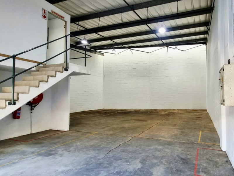 Spacious industrial warehouse unit featuring high ceilings with exposed steel trusses, concrete flooring, and an internal staircase leading to an elevated office area.
