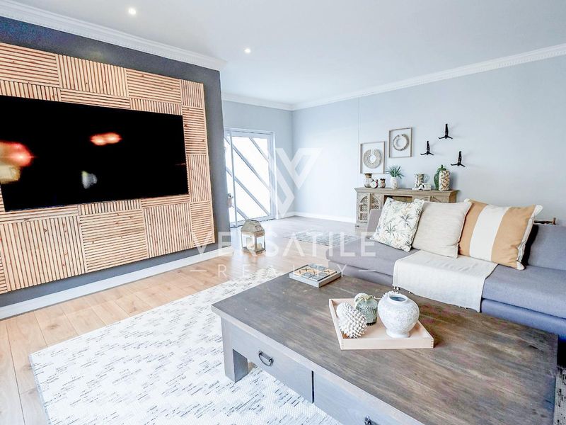 A modern living room featuring a custom timber slat feature wall, recessed downlighting, and light-toned laminate flooring with access to an outdoor area.