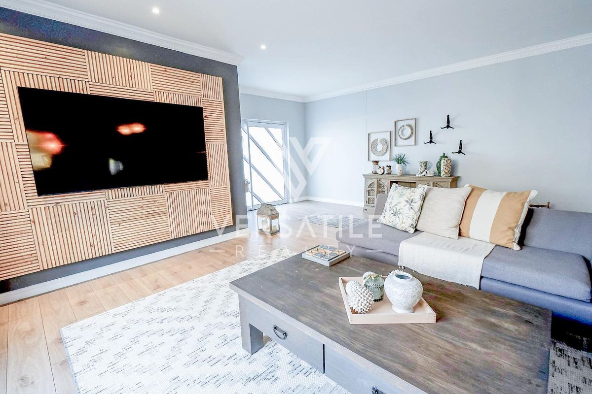 A modern living room featuring a custom timber slat feature wall, recessed downlighting, and light-toned laminate flooring with access to an outdoor area.